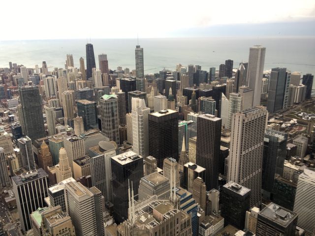 Aerial view showcasing Chicago downtown skyline with numerous skyscrapers next to Lake Michigan. Urban architecture and layout prominent under a cloudy sky. Useful for articles on urban planning, travel guides, business presentations, and tourism-related content featuring American cities.