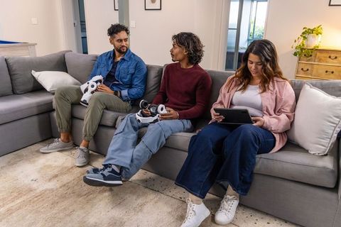 Diverse friends playing virtual reality gaming on gray sectional sofa with controllers