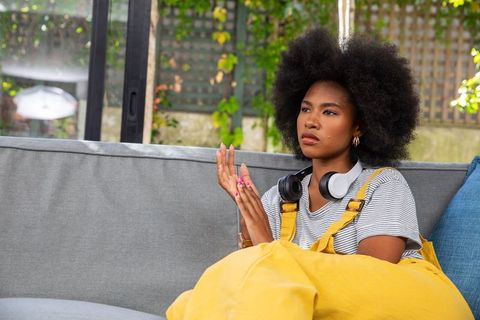 Young woman relaxing on sofa with yellow overalls and headphones
