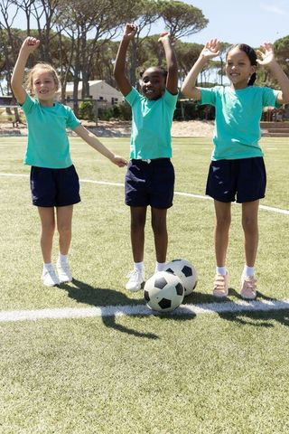Diverse girls celebrating on soccer field raising arms, youth team spirit and teamwork