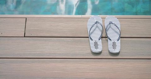 Striped flip-flops sitting on light composite deck beside turquoise pool edge, summer copy space