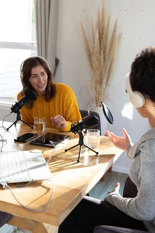 Female podcasters recording conversational interview in home studio with microphones