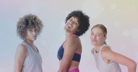 Three women smiling and posing in pastel fitness portrait, diverse active lifestyle trio