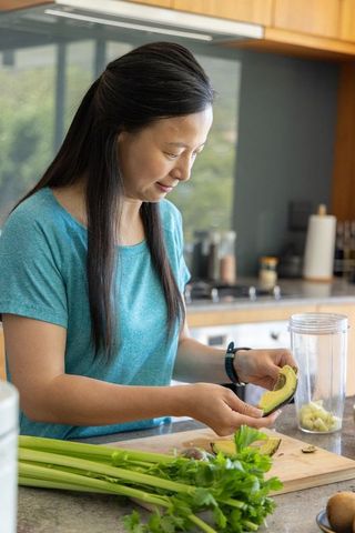 Preparing avocado smoothie in bright home kitchen with fresh celery and blender
