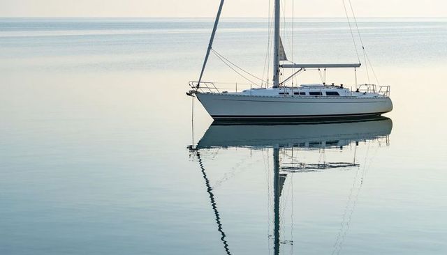 White sailboat floating on glassy sea reflecting mast and hull at dawn minimalist calm