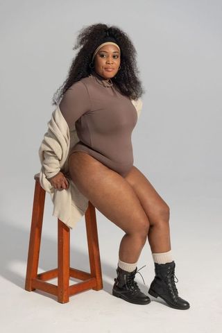 Confident plus-size african american woman posing on wooden stool in neutral studio