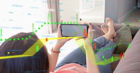 Mid-adult asian woman reclining on sofa holding smartphone viewing stock trading charts