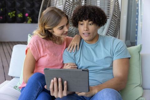Young couple relaxing on balcony couch watching tablet together, casual lifestyle