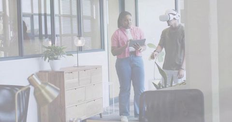 Colleagues testing virtual reality headset while woman guides with tablet in modern office