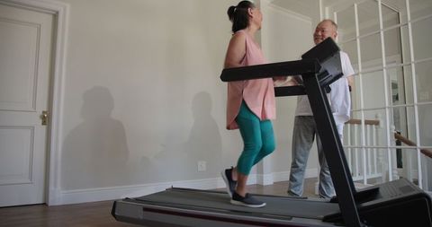Asian woman exercising on treadmill with encouragement from man