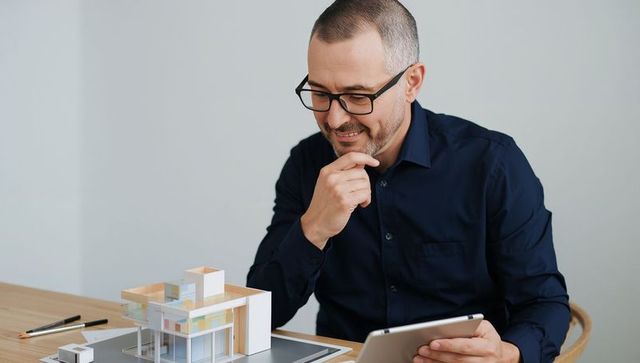 Architect examining modern scale model while using tablet in studio workspace