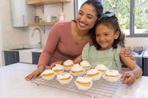 Mother and Daughter Smiling Presenting Frosted Cupcakes on Marble Countertop in Kitchen