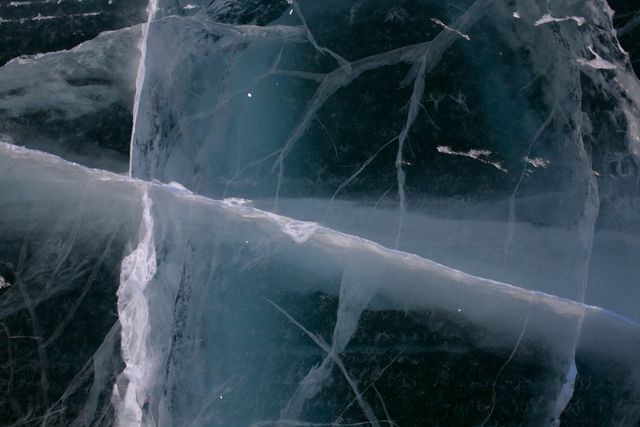 Cracked ice surface with deep blue hues showcasing natural patterns. Perfect for use in winter-themed designs, nature studies, environmental awareness projects, or as abstract backgrounds for various applications.