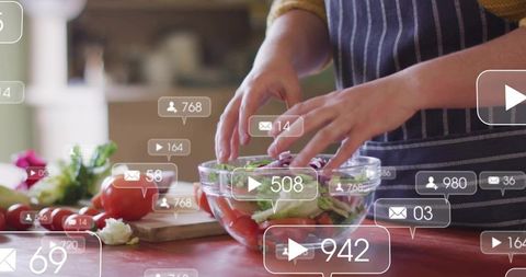 Woman tossing fresh salad in glass bowl on red countertop with social media overlays