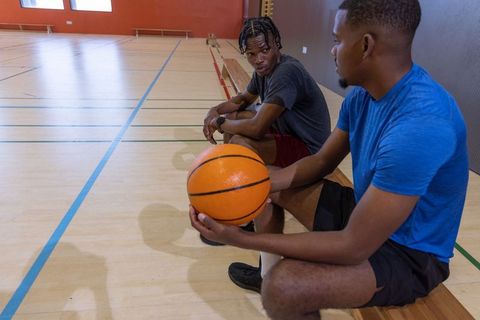 African american men resting on gym bench holding basketball and discussing game strategy