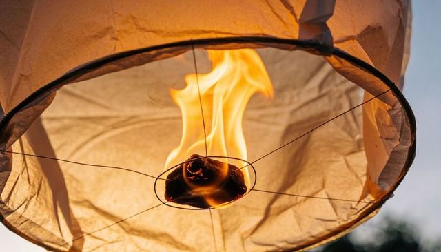 Burning sky lantern closeup glowing flame over fuel pad and wire frame at dusk