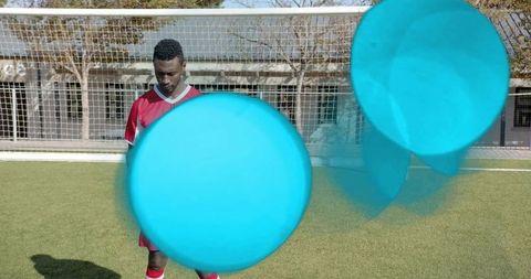 Standing soccer player facing regulation goal with cyan motion orbs on sunny turf