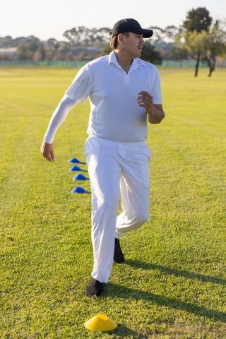 Cricket player sprinting through agility cones on sunlit grassy training field