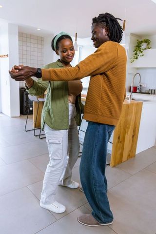 African american couple dancing together in bright modern kitchen near wooden island