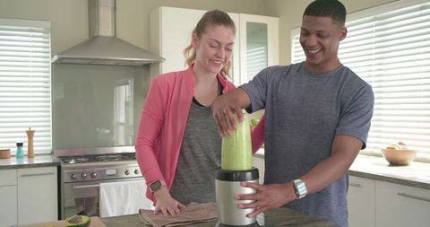 Couple making green smoothie on kitchen island in sportswear and smartwatch
