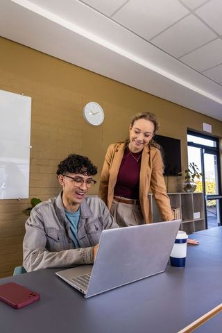 Young coworkers collaborating over laptop in modern office with warm tones