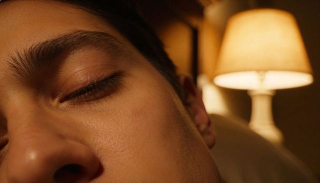 Intimate close-up of man resting by warm bedside lamp light, nighttime relaxation