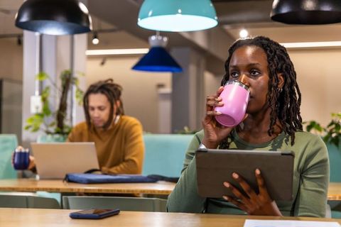 Diverse professionals coworking in modern cafe workspace sipping coffee and using tablet