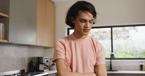 Young person wearing pink top and pearl necklace standing in bright modern kitchen
