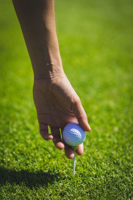 Close up of hand keeping golf ball on tee at golf course. sports and active lifestyle concept.
