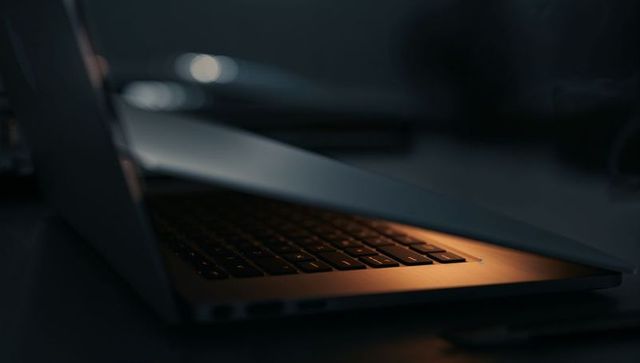 Half-closed laptop with warm backlit keyboard emitting moody amber glow