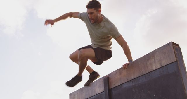 A young Caucasian man is actively engaged in parkour, leaping from a high wall, with copy space - Download Free Stock Photos Pikwizard.com