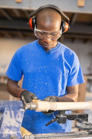 African american woodworker shaping wooden spindle on lathe wearing safety gear