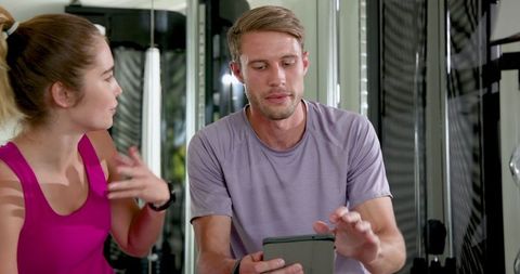 Motivated couple discussing workout plan in gym with tablet