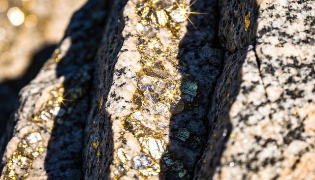 Catching sunlight on quartz vein revealing iridescent metallic flecks in grooved bedrock