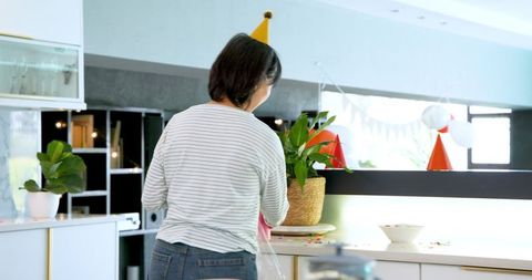 Senior woman tidying kitchen after birthday celebration cleanup routine