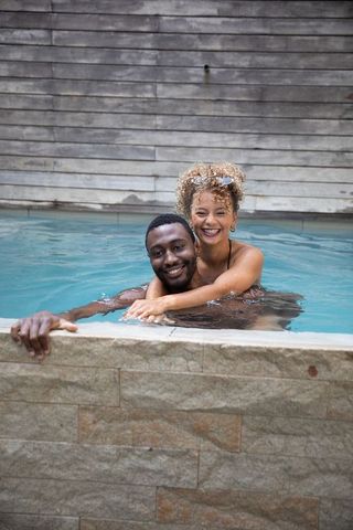 Mixed-race woman embracing black man in backyard pool, smiling and relaxing