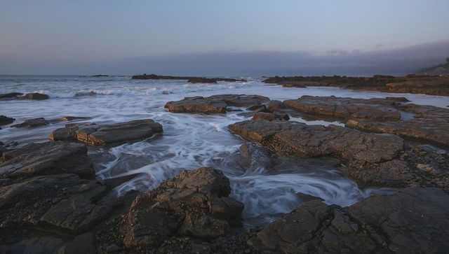 Rugged rocky coast with foamy tidal channels at dusk, sweeping long-exposure seascape