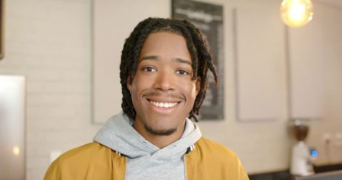 African american man smiling in cozy cafe wearing mustard jacket and gray hoodie