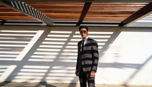 Businessman under pergola casting linear shadows on white wall, modern minimalist portrait