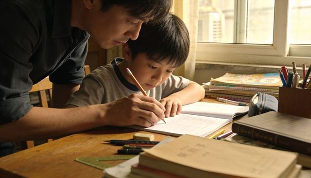 Father guiding son writing homework at desk in warm natural light