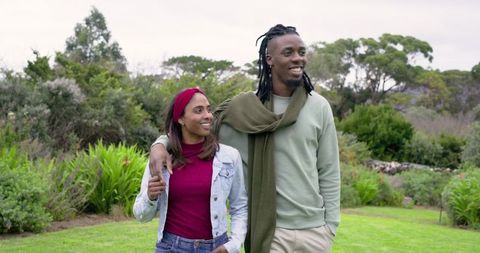 Diverse couple strolling on lush garden lawn smiling and embracing in casual outfits