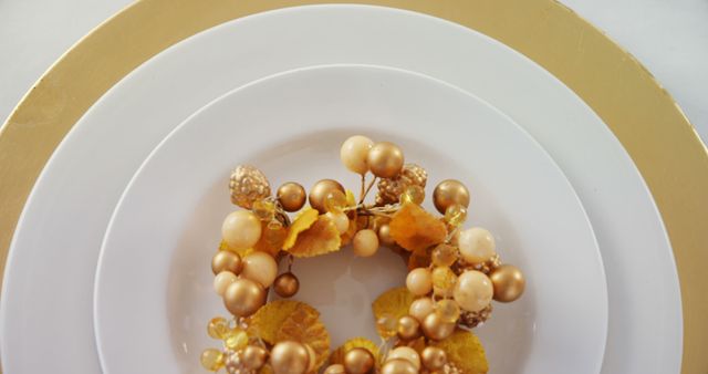 A golden napkin ring adorned with pearls and leaves is placed on a white plate with a gold rim, with copy space. The elegant table setting suggests a festive or formal dining occasion.
