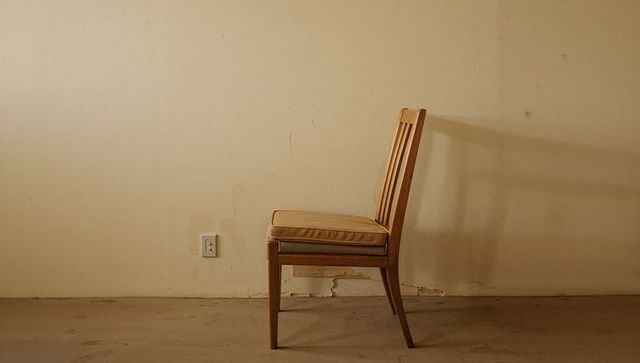 Standing wooden chair casting shadow against peeling plaster wall with empty copy space