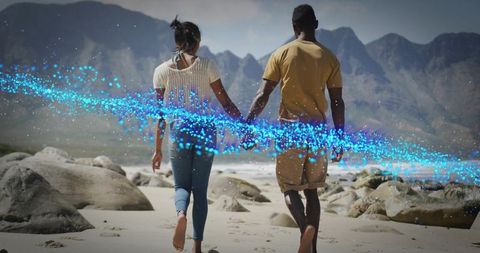 Couple walking hand-in-hand on rocky beach with blue particle light trail, romantic seascape