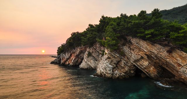 Peaceful coastal scene featuring a stunning rocky cliff adorned with lush pine trees, with a beautiful sunset casting warm colors over the ocean. Ideal for travel and tourism promotions, nature and landscape illustrations, serene and tranquil themed projects, and environmental awareness campaigns.