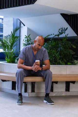 African american healthcare worker taking coffee break in lobby checking smartwatch