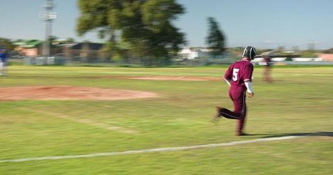 Male Baseball Teammates Sprinting in Maroon Gear on Field