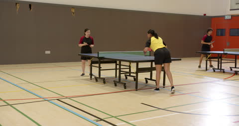 Students Competing in Dynamic Table Tennis Match in Gymnasium