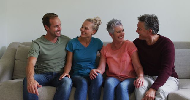 Close group of friends sitting on couch smiling and chatting. Perfect for concepts involving friendship, social interactions, indoor leisure activities, and casual gatherings. Can be used in lifestyle blogs, friendship day promotions, and articles about maintaining relationships.