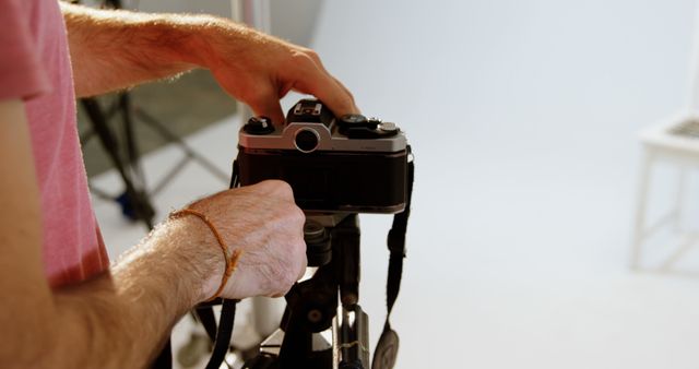 A Caucasian man adjusts a vintage camera on a tripod, with copy space. His focus on the equipment suggests a passion for photography or a professional setting.